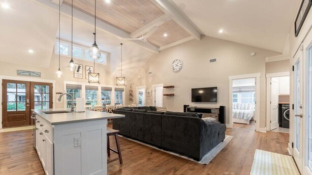A spacious living area with a large island, dark grey sofa, and a flat-screen TV. - Luxury St. Simons Island Vacation Rental | Private Pool Near Pier Village (Saint Simons Island)