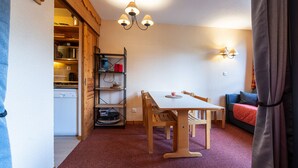 Une pièce compacte comprenant une table à manger en bois, des chaises, un petit coin cuisine et un espace salon confortable avec un canapé.