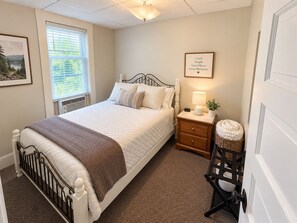 A neatly arranged bedroom with a bed, bedside table, lamp, and a framed inspirational quote on the wall.