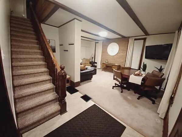 A staircase leading to a living area with a sofa, a dining table, and a TV mounted on the wall.