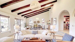 Un salon spacieux avec un canapé blanc, une table basse en bois et un fauteuil bleu. On aperçoit à l’arrière-plan un coin repas avec une table et des chaises.