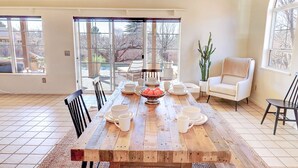 Un coin repas avec une table en bois dressée pour le repas, entourée de chaises, et une grande fenêtre donnant sur l’extérieur.
