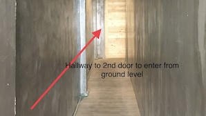 A narrow hallway with a wooden door at the end, marked by a red arrow indicating the direction to the second door from the ground level.
