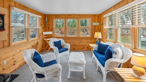 Ein gemütliches Zimmer mit Holzwänden und großen Fenstern, ausgestattet mit Korbmöbeln und einem kleinen Tisch.