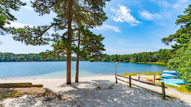 Ein Strand mit einer Holzlattenveranda, einer Reihe von Kanus und einem stillen See, der von Bäumen umgeben ist.