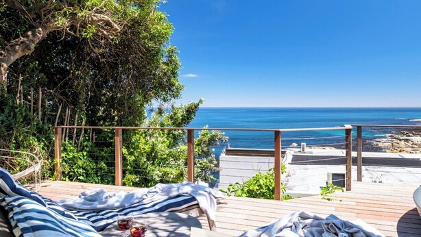 Une terrasse avec des chaises longues, un livre et des verres de boissons, offrant une vue sur la côte.