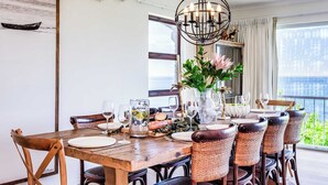 Un coin repas avec une table en bois, des chaises en osier, un lustre et une vue sur l’extérieur.