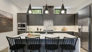Una cucina moderna con isola centrale, sedie nere, elettrodomestici in acciaio inossidabile e illuminazione a sospensione.