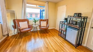 A room with wooden flooring, two brown leather chairs, a small round table with a vase, a window with curtains, and a kitchenette with a microwave and coffee maker. - Poolside studio in the Foothills with Pool + Hot tub
 (Tucson)
