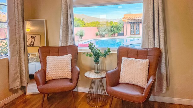 A room with two brown leather chairs with white cushions, a small round table with a vase, and a window with curtains. - Poolside studio in the Foothills with Pool + Hot tub
 (Tucson)