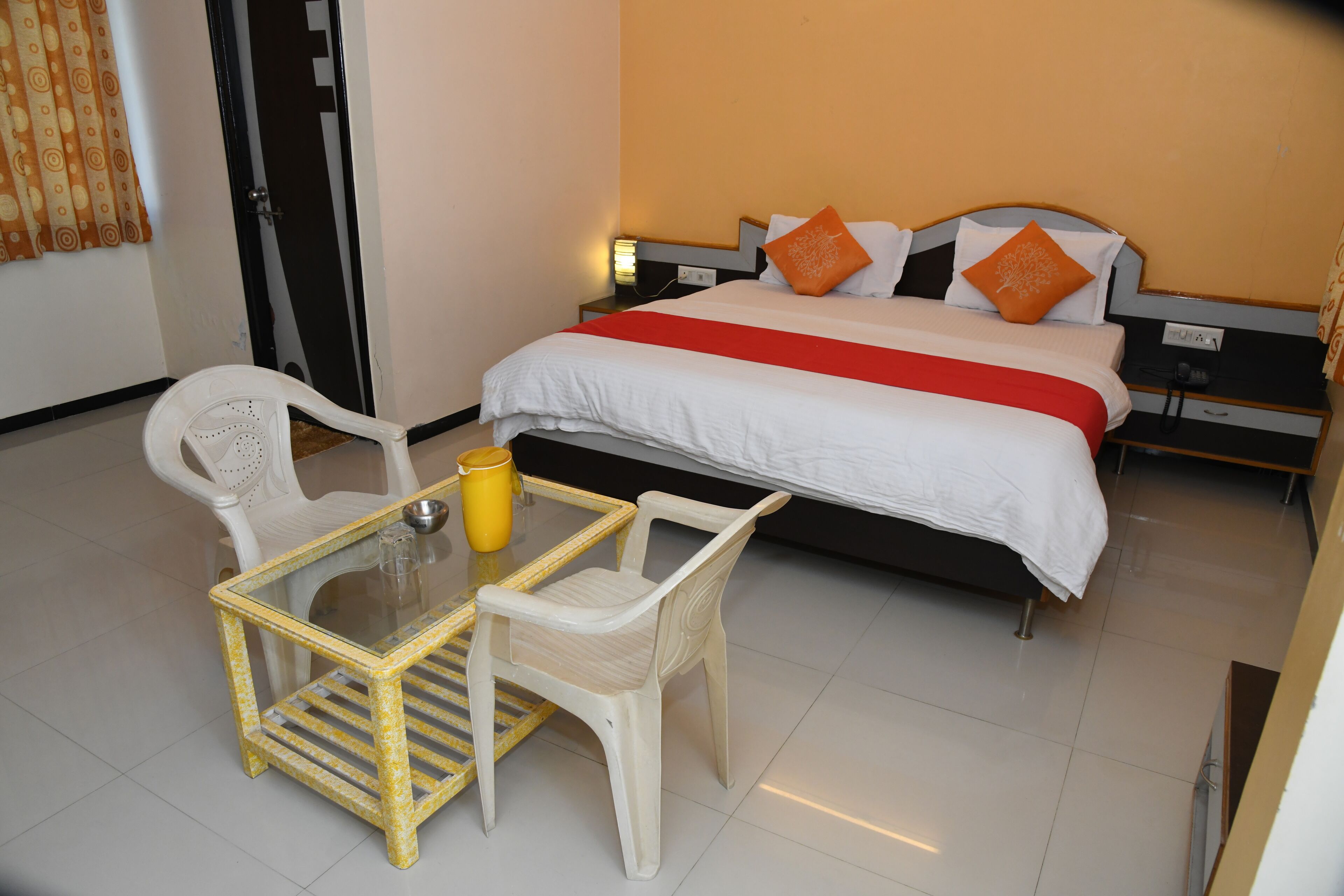 Une chambre d’hôtel avec un lit, une table de chevet, une table en verre avec des chaises et une porte.