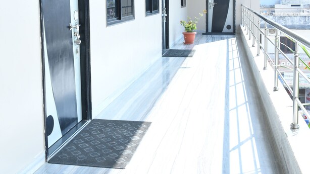 A corridor with doors, windows, a potted plant, and a metal railing. - Hotel durga (Abu Road)