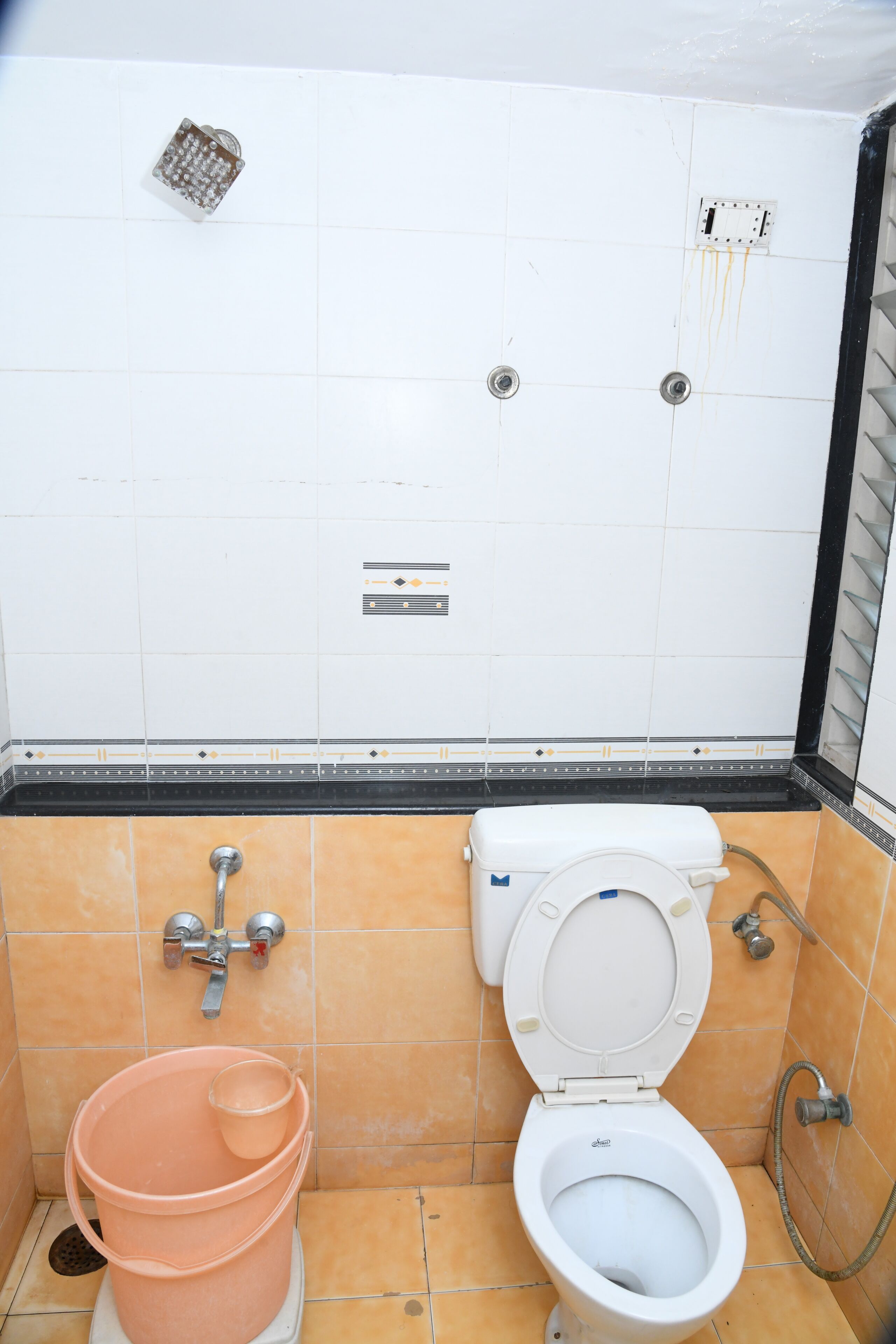 Een badkamer met een toilet, een roze emmer en een doucheput.