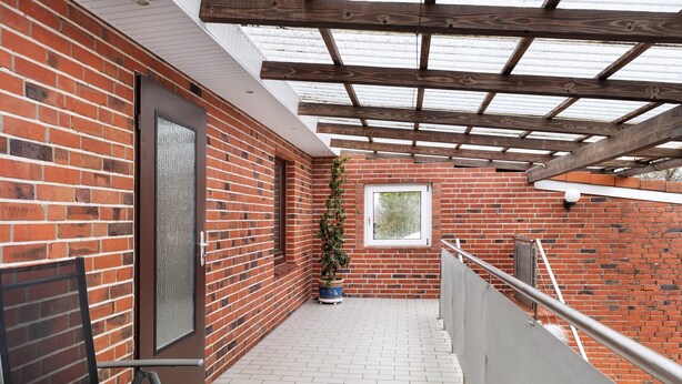 A covered outdoor area with a brick wall, a door, a window, and a potted plant. - Apartment 'Landferien Schütt' with Balcony (Neuenkirchen)