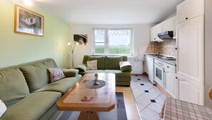 A living room with a sofa, a coffee table, and a view of the outdoors through a window. - Apartment 'Landferien Schütt' with Balcony (Neuenkirchen)