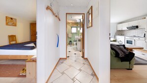 A narrow hallway leading to a bedroom with a bed, a small table, and a pair of yellow slippers. - Apartment 'Landferien Schütt' with Balcony (Neuenkirchen)