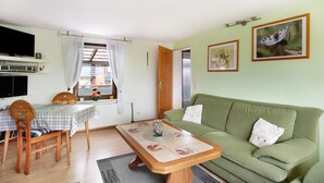 A living room with a green sofa, a wooden coffee table, a dining table with chairs, a TV, and framed pictures on the wall. - Apartment 'Landferien Schütt' with Balcony (Neuenkirchen)