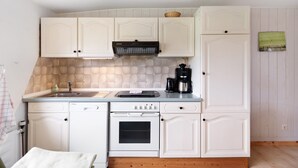 A kitchen with white cabinets, a stove, a sink, and a coffee maker. - Apartment 'Landferien Schütt' with Balcony (Neuenkirchen)