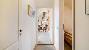 Een hal met een deur aan de linkerkant, een bed aan de rechterkant en een eethoek op de achtergrond.