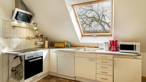 Een keuken met een inbouwoven, vaatwasser, magnetron en een raam met uitzicht op een boom.