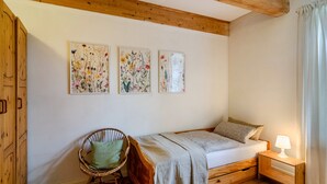 Un dormitorio con una cama de madera, una silla, una mesita de noche y tres cuadros florales en la pared.
