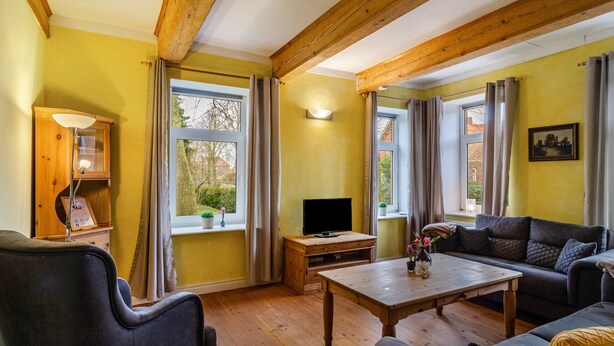 Una sala de estar con vigas de madera, un sofá, una mesa de centro, un televisor y una ventana con cortinas.