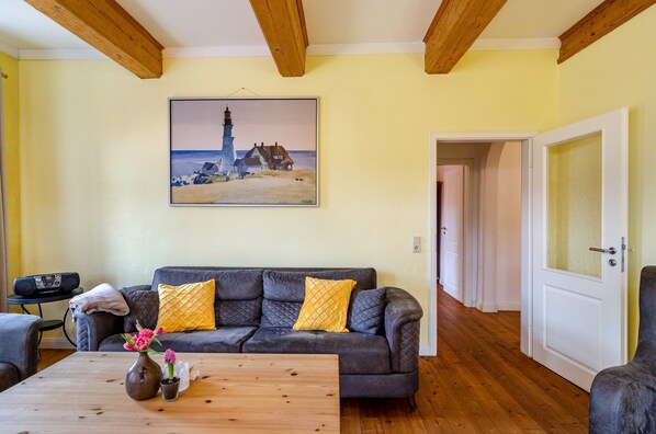 A living room with a couch, a wooden coffee table, a painting of a lighthouse, and a door leading to another room.