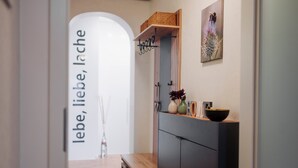 Un couloir avec un banc en bois, une armoire noire et une étagère murale ornée d’objets décoratifs.