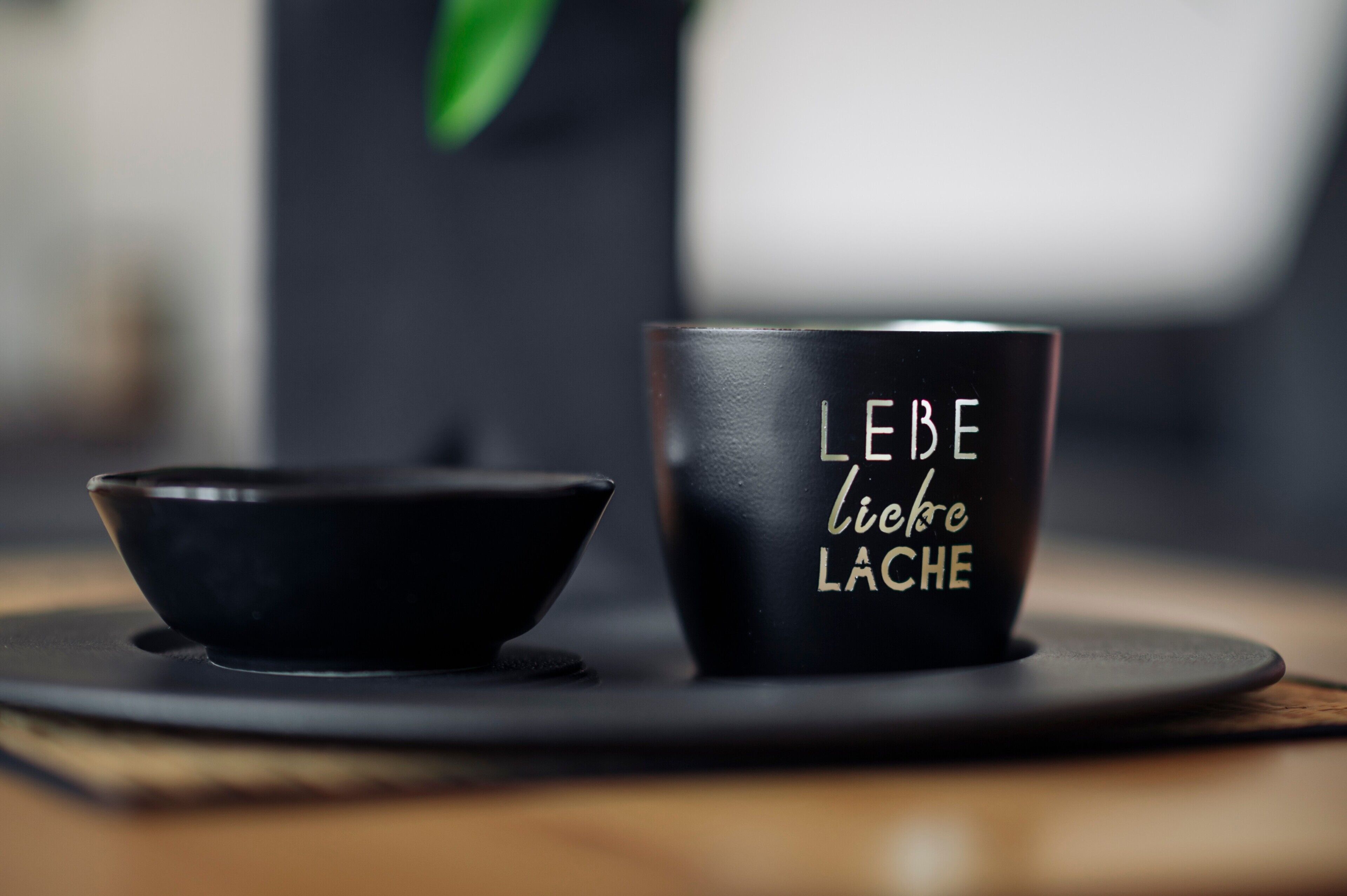 Een zwarte mok met de tekst 'LEBE liebe LACHE' en een zwarte kom op een rond zwart bord.