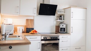 Une cuisine moderne avec des meubles blancs, un four encastré, une machine à café et un panier de fruits posé sur le plan de travail.