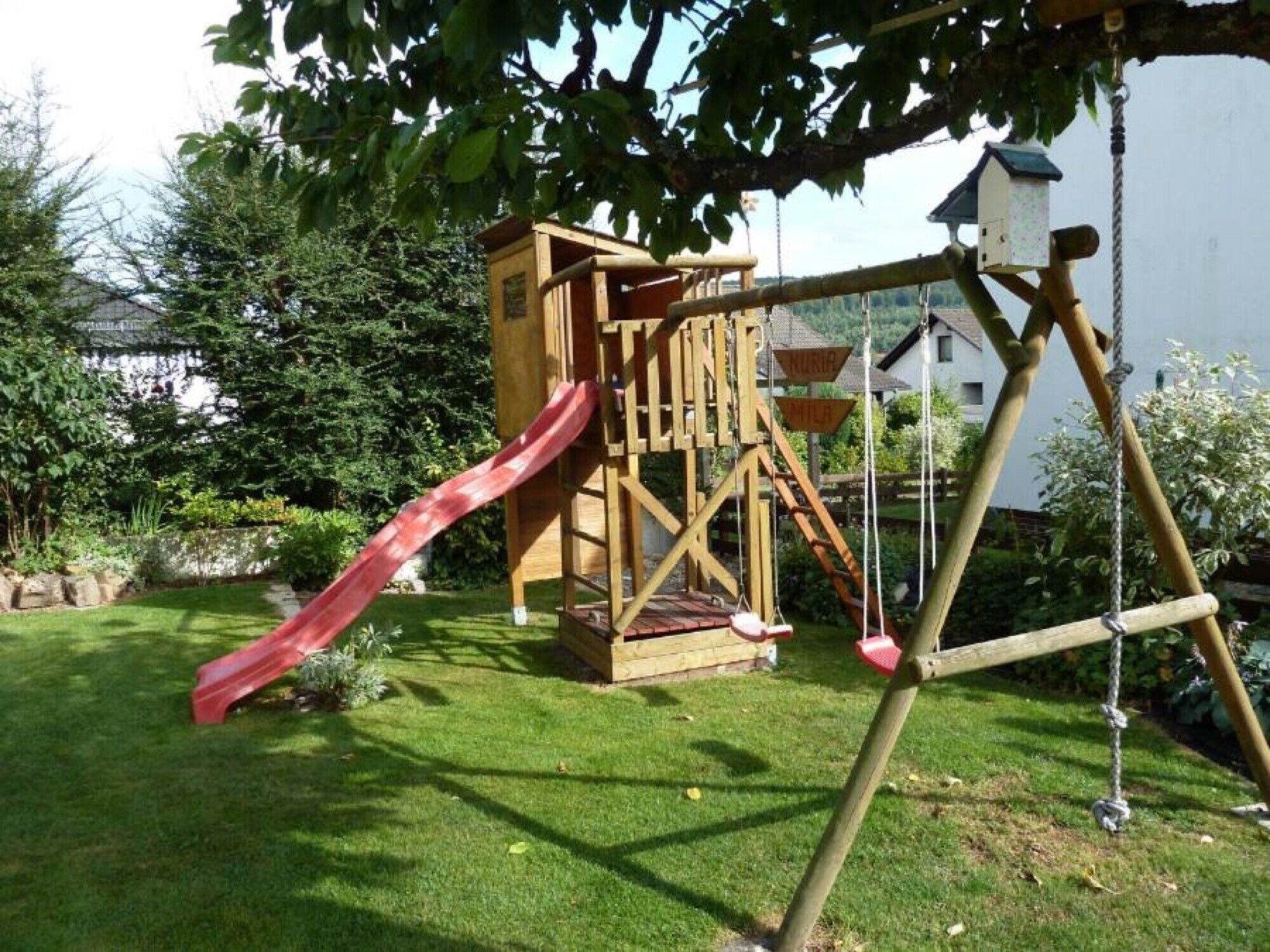 A wooden play structure with a slide and swings in a grassy yard.