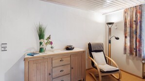 Una habitación con un armario de madera, una silla, una lámpara de pie y una cortina.