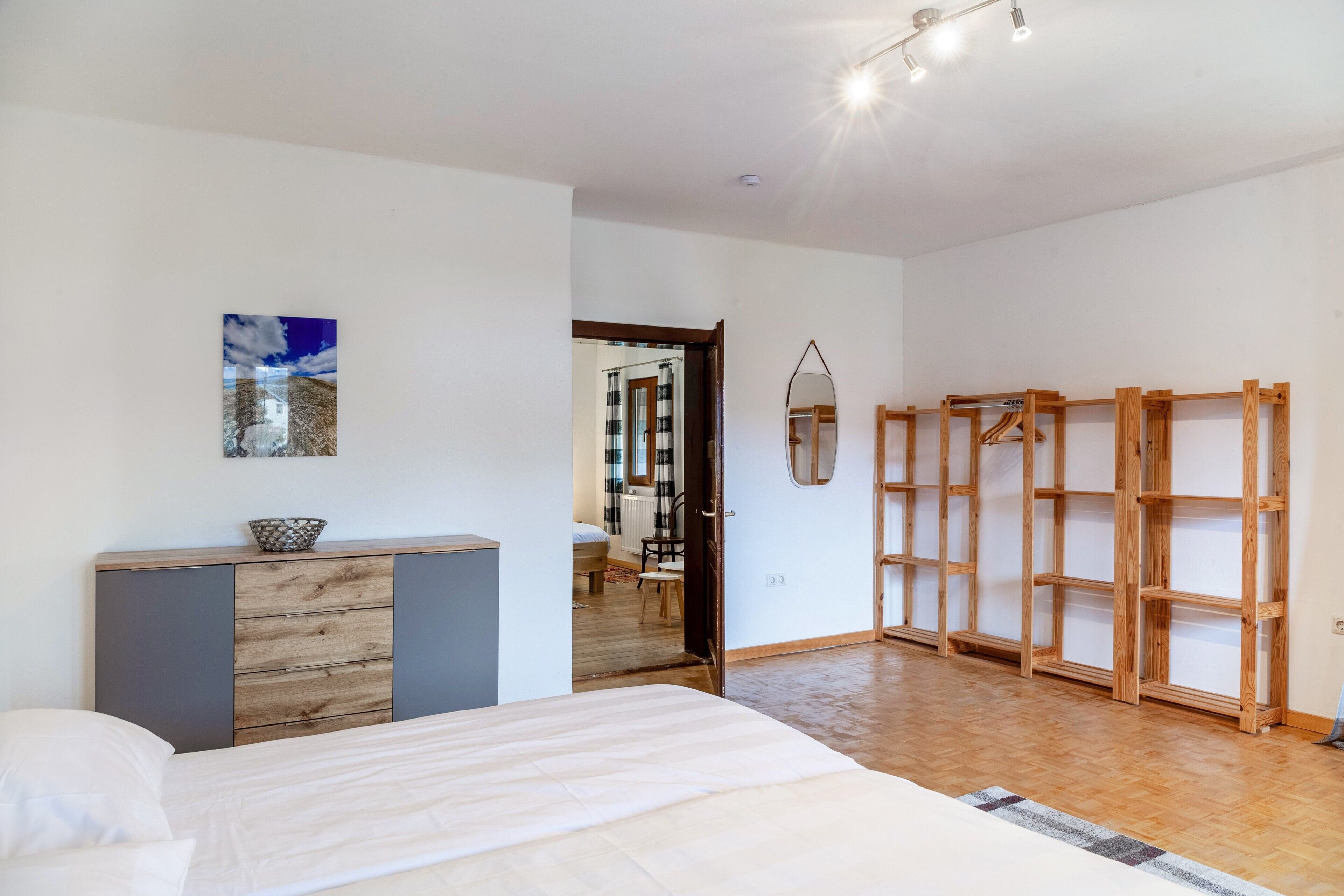 A bedroom with a bed, a dresser, a mirror, and a wooden shelving unit.