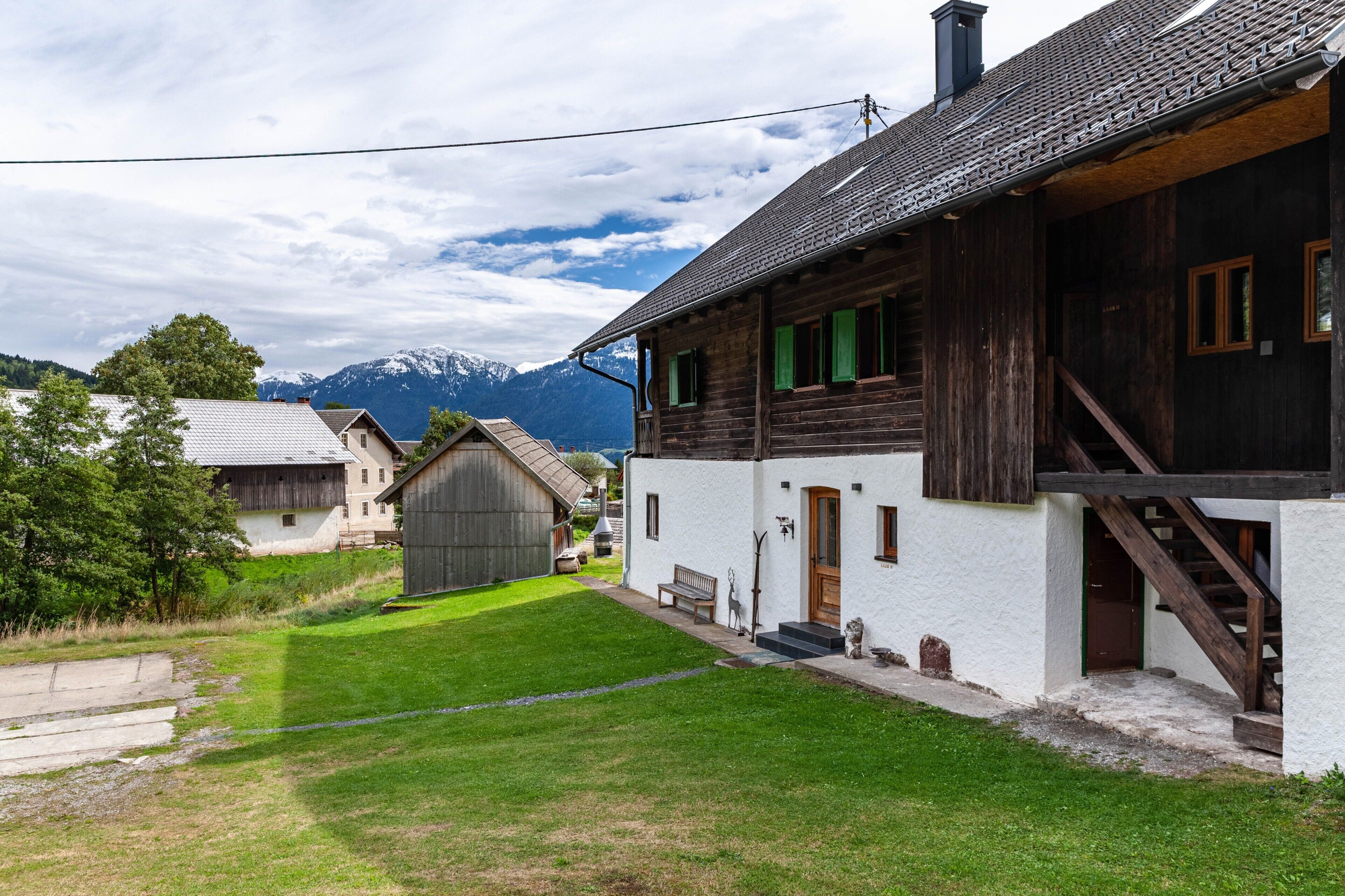 Una casa rústica de madera con fachada blanca, una escalera de madera y un banco en el exterior.