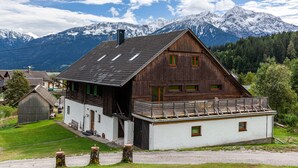 Een houten huis met een schuin dak, een balkon en uitzicht op besneeuwde bergen.