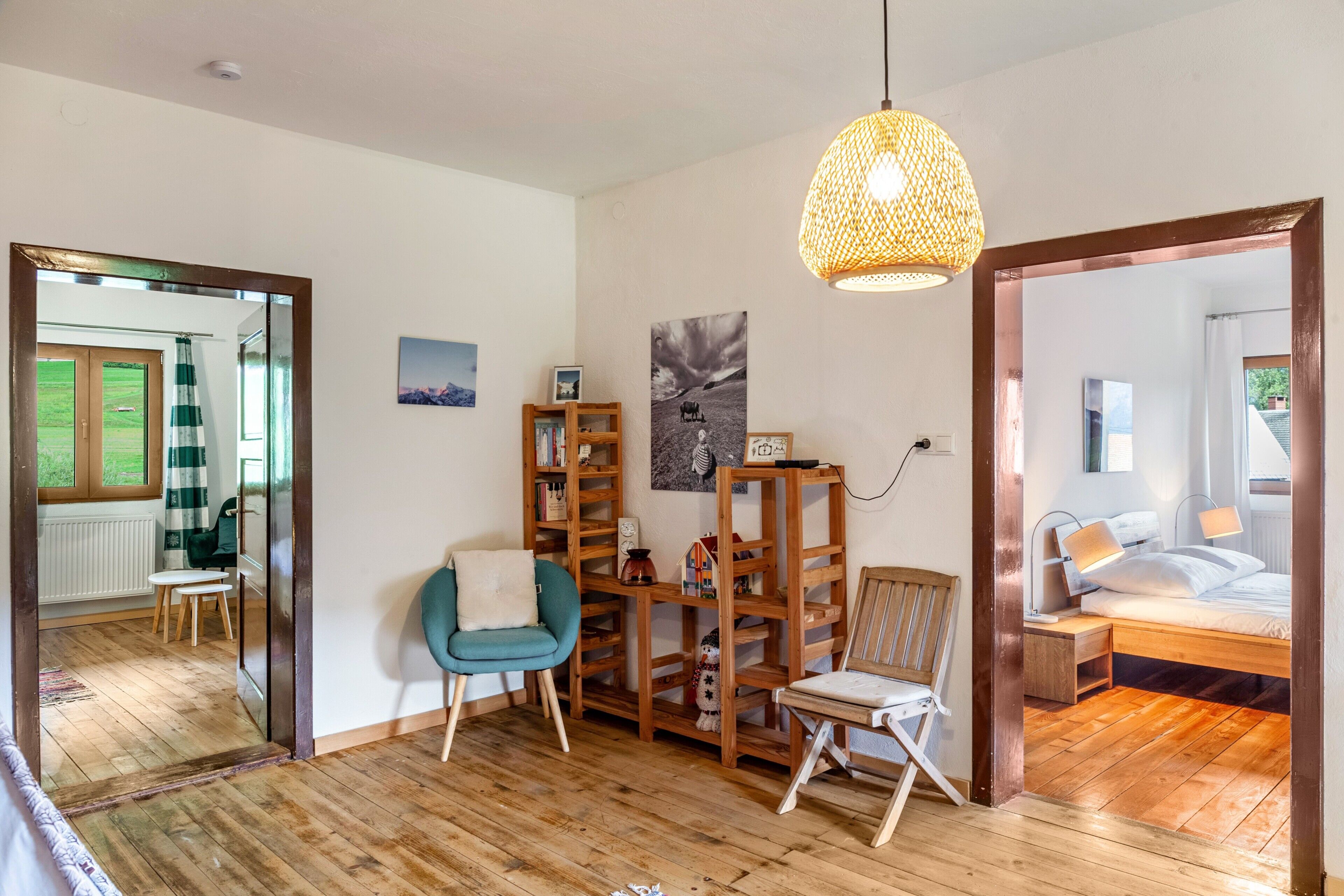 Ein Zimmer mit Holzboden, einer Spiegelwand, einem blauen Sessel, einem Holzregal und einem Bett mit Nachtschränkchen.