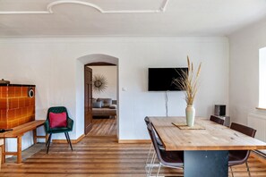 A dining area with a wooden table, chairs, a bench, a TV mounted on the wall, and a vase with dried plants.