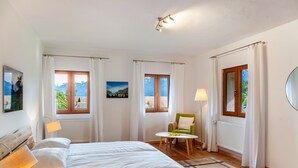 Een slaapkamer met een bed, twee ramen, een stoel, een lamp en uitzicht op het landschap.