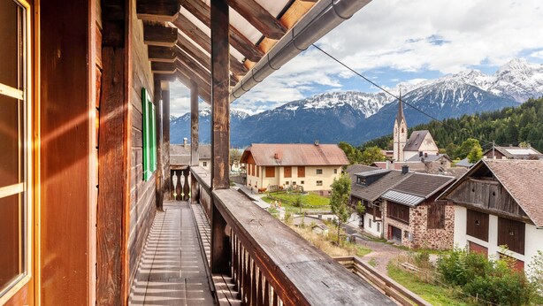Een houten balkon met uitzicht op een bergketen en traditionele gebouwen.