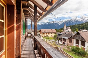 Een houten balkon met uitzicht op een bergketen en traditionele gebouwen.