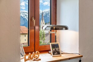 Ein Fenster mit Holzrahmen, ein Schreibtisch mit Lampe, ein Bilderrahmen und hölzerne Lettern, die ‚LAAS‘ schreiben.