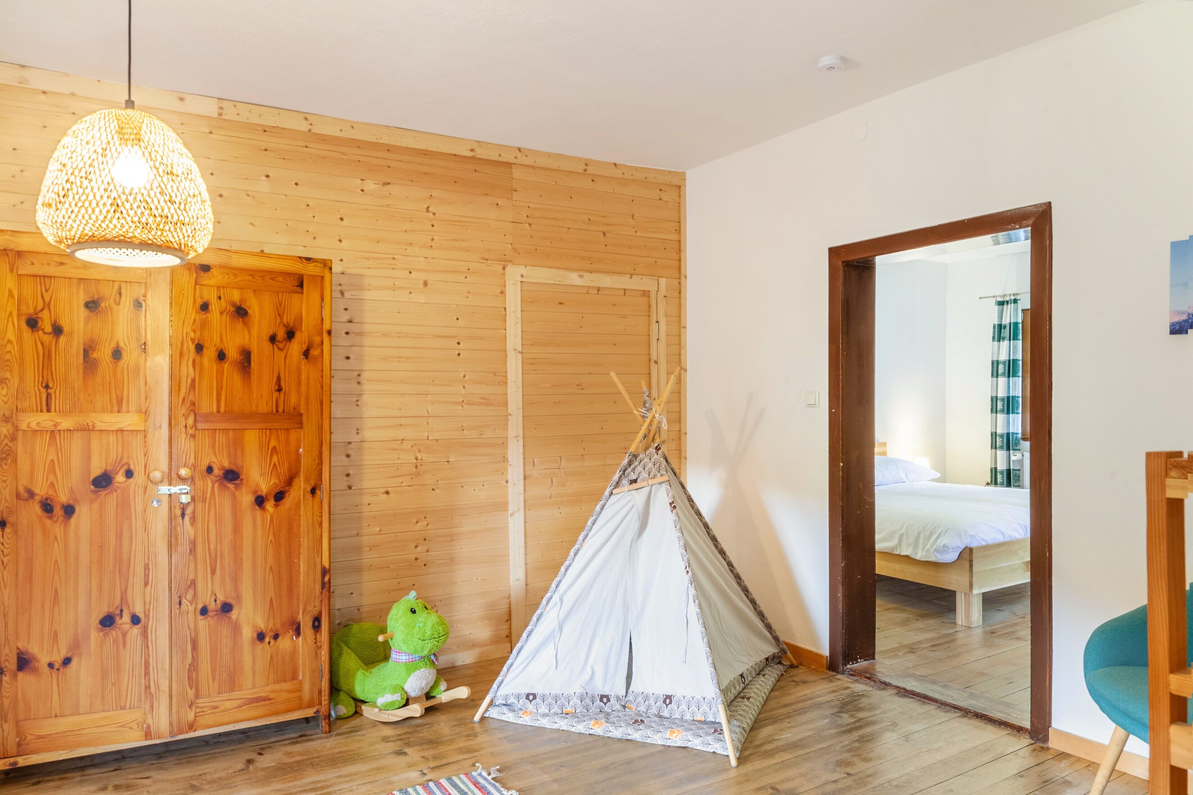 Ein Zimmer mit Holzwänden, einem Bett, einer grünen Froschfigur, einer Hängelampe und einem Zelt.