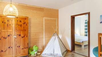 Ein Zimmer mit Holzwänden, einem Bett, einer grünen Froschfigur, einer Hängelampe und einem Zelt.