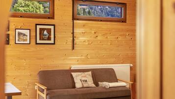Ein Holzblockhaus-Innenraum mit einer Couch, gerahmten Bildern und zwei Fenstern.