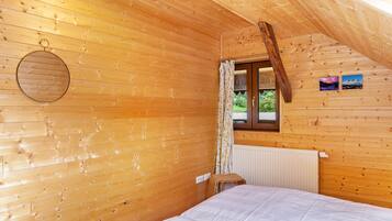 Una camera di una baita in legno con un letto, una finestra con tende, un termosifone e un quadro appeso al muro.