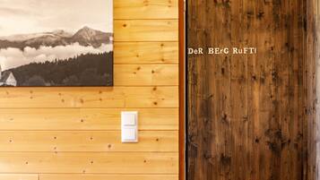 Un interior de madera con un interruptor de luz en la pared, una puerta de madera y un cuadro enmarcado de un paisaje montañoso.