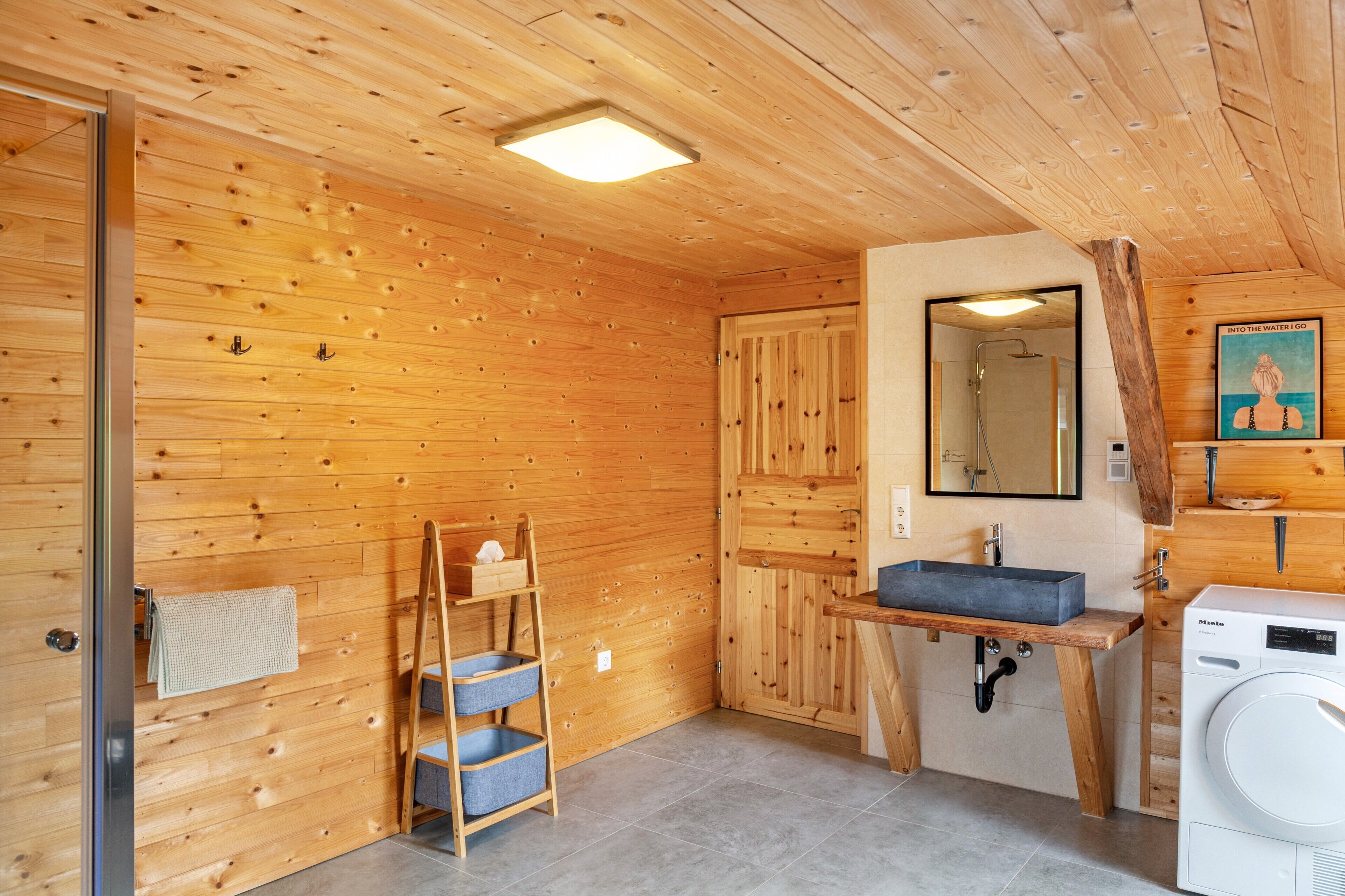 Un intérieur en bois avec un plancher en bois, un évier, un miroir, une machine à laver et une échelle.
