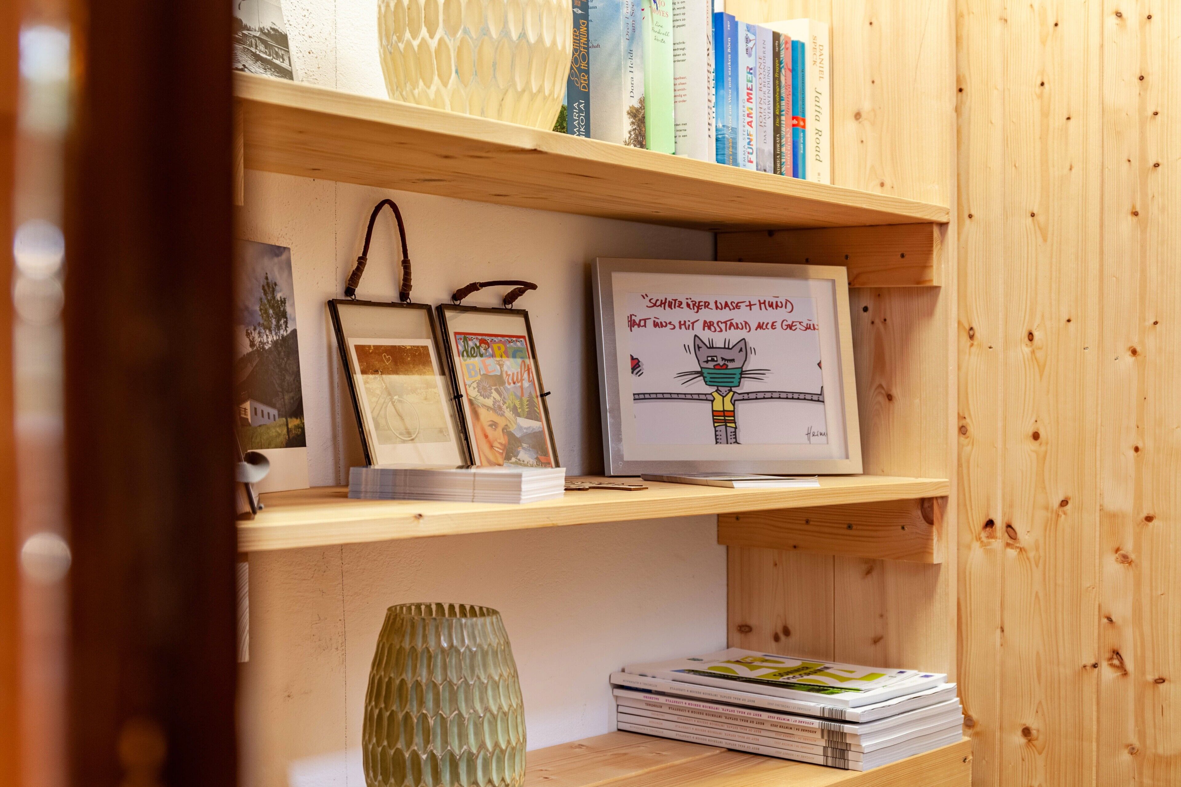 Een houten boekenplank met boeken, ingelijste foto's en een decoratieve vaas.