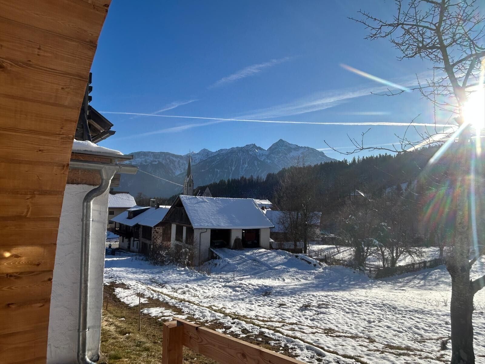 Edifici de fusta amb un paisatge cobert de neu, una església i muntanyes al fons.