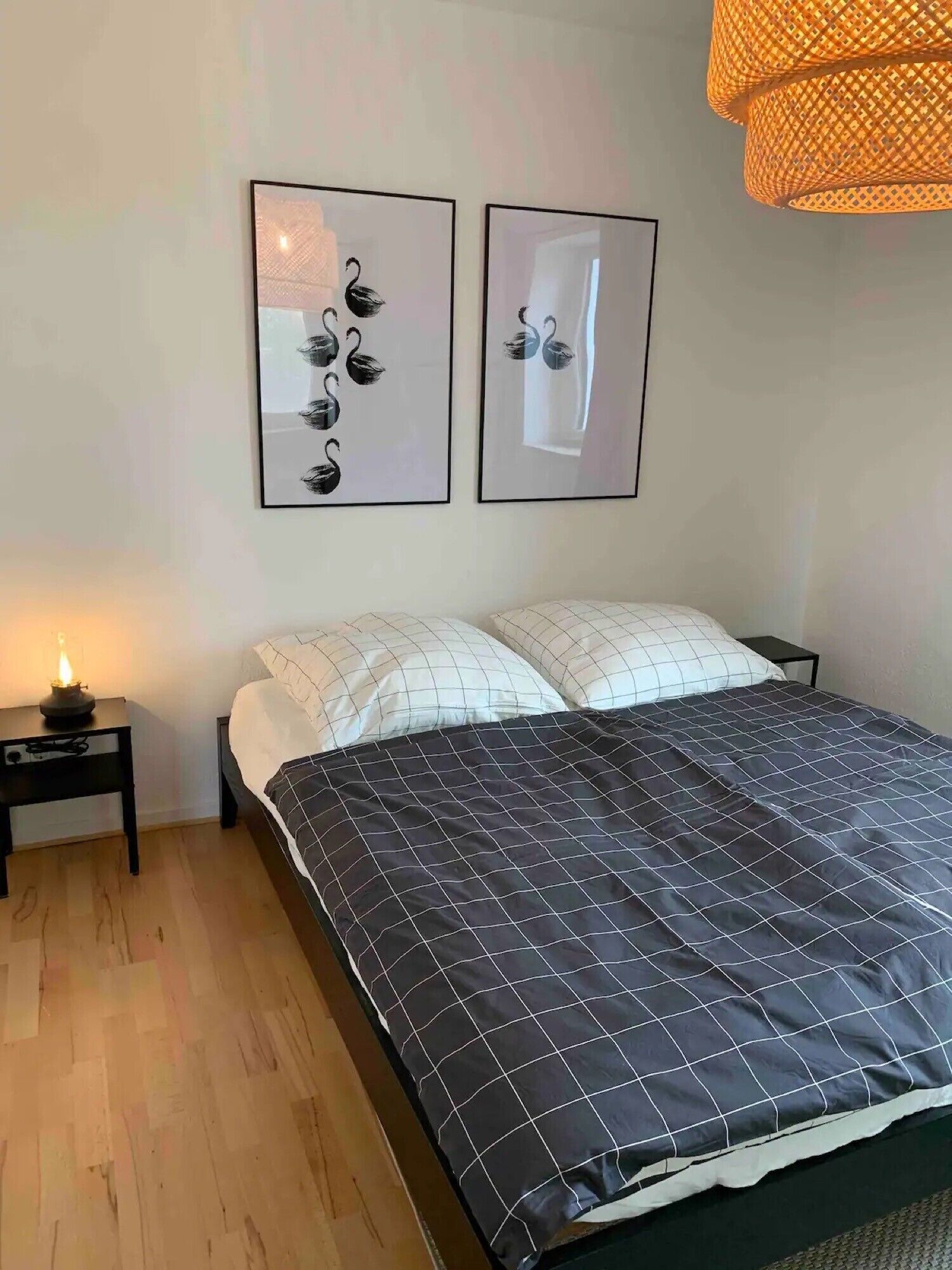 A bedroom with a bed, two bedside tables, a nightstand, and a hanging light fixture.